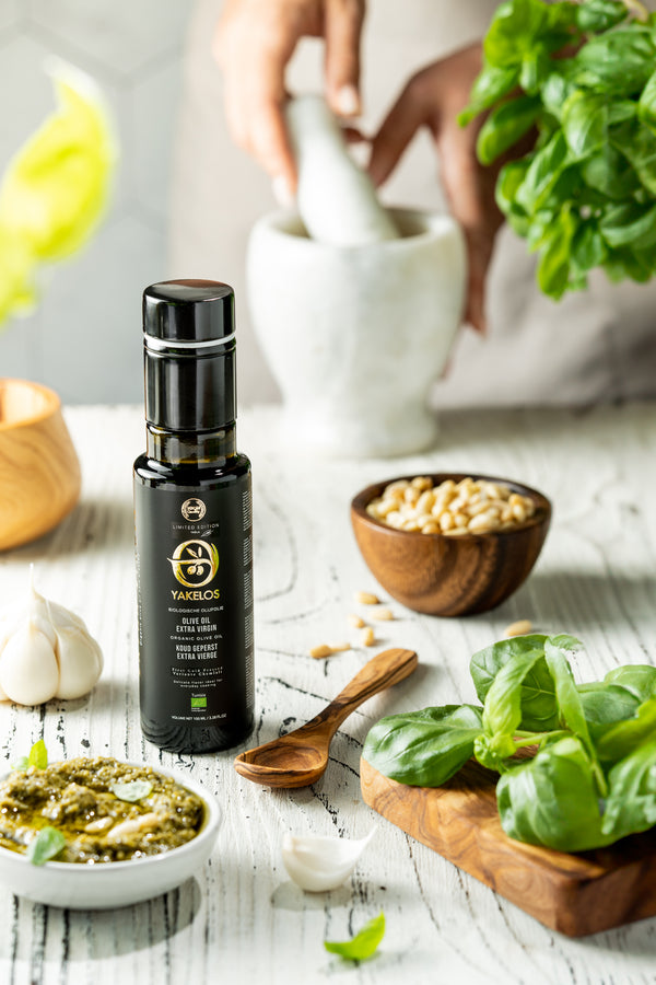 Fles Yakelos biologische extra vierge olijfolie 100ml op tafel met pesto, basilicum, pijnboompitten en knoflook